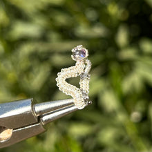 Load image into Gallery viewer, intricately hand wire wrapped silver Vipera Serpent Pierceless Nose Cuff with a prong set rose de France purple amethyst cabochon displayed on a metal holder against a blurred greenery background.