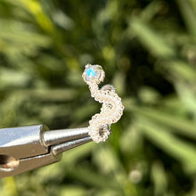 Load image into Gallery viewer, intricately hand wire wrapped silver Vipera Serpent Pierceless Nose Cuff with a prong set gray labradorite cabochon displayed on a metal holder against a blurred greenery background.