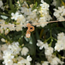 Load image into Gallery viewer, intricately hand wire wrapped gold Vipera Serpent Pierceless Nose Cuff with a prong set white rainbow moonstone cabochon displayed on a metal holder against a blurred greenery background.